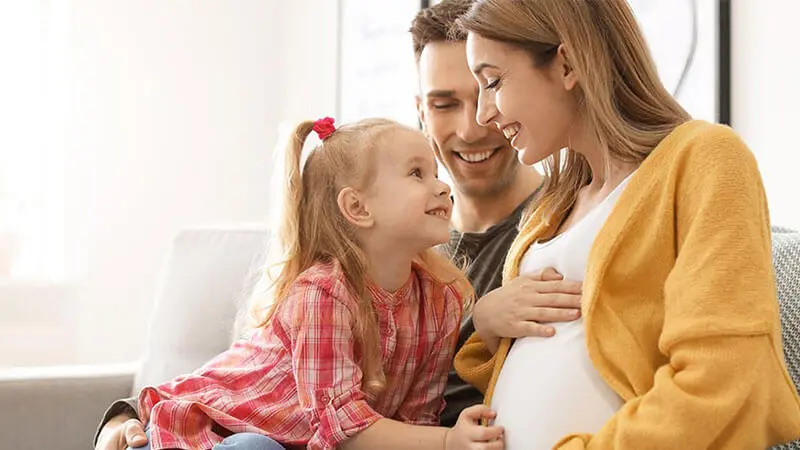 Familia joven relajada en un sofá anticipando la llegada de su nuevo bebé