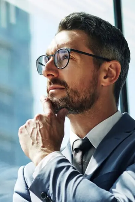 Man wearing a suit and glasses looking out an office window