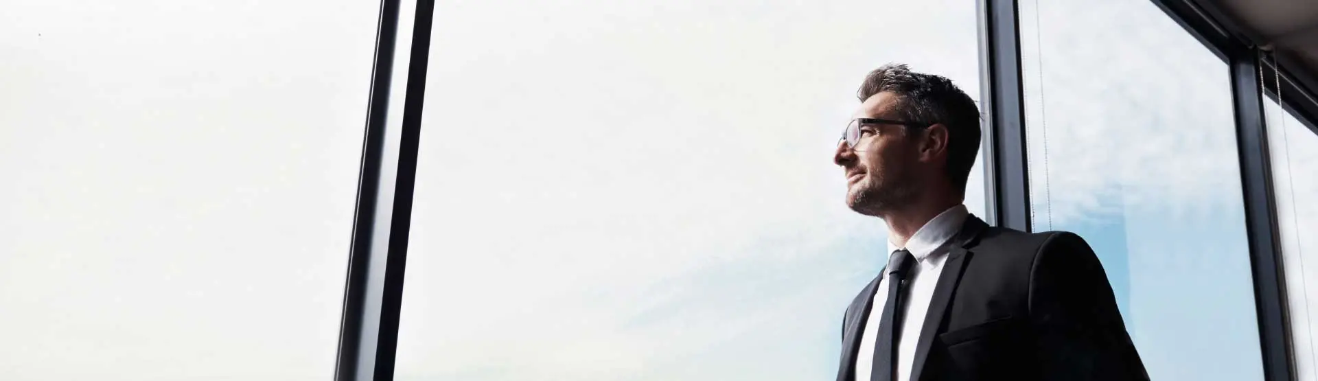 Man in suit and tie gazing out a large window