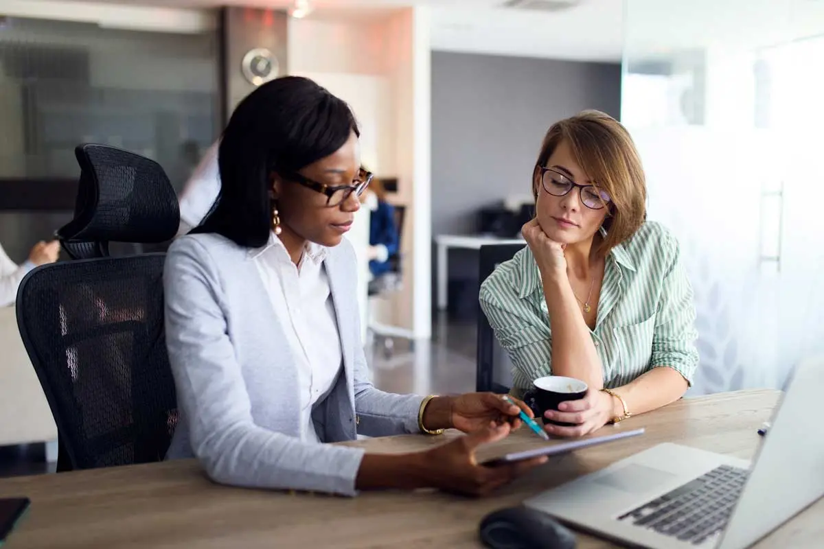 Two professional women in a conference room looking at a mobile device