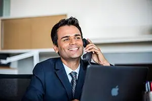 Man wearing a suit sitting at his desk holding a phone talking to a client