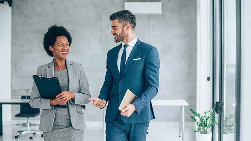 Man and woman wearing business suits and talking as they walk through their office