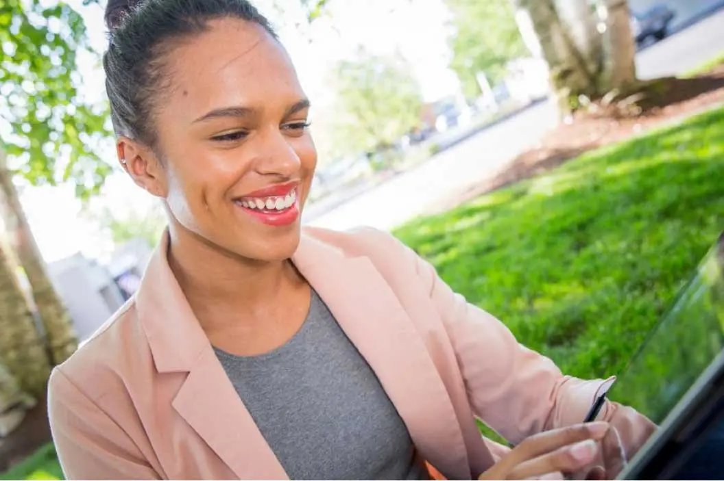 Woman sitting outdoors at a table in a park and using a tablet to make a payment.