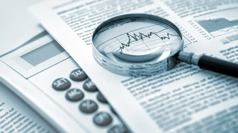 Magnifying glass on top of a newspaper and calculator