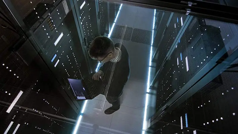 Man standing in a server room with a laptop looking at operating lease vs financing lease for equipment lending options.