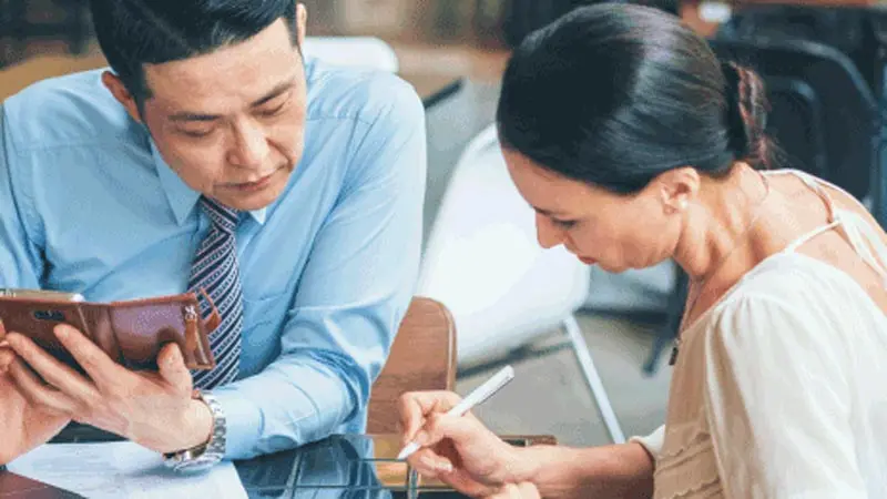 Man wearing a tie sitting with a woman who is writing notes about B2B payments