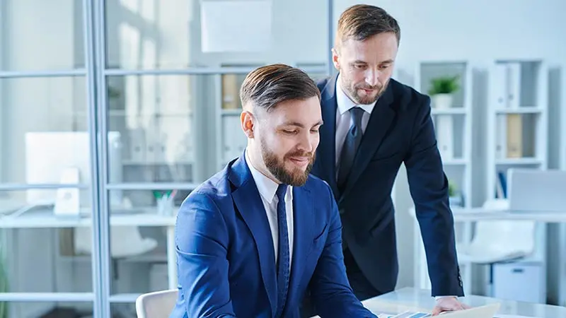 Two young professional men wearing suits and looking at collateral loans on a computer