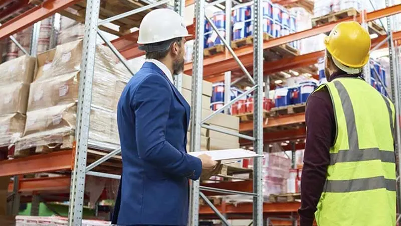 Two warehouse workers in hardhats looking at inventory for commodity derivatives