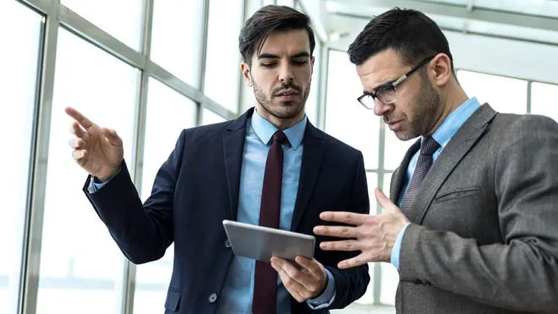 Two businessmen with a tablet discussing the advantages of digital supplier payments.