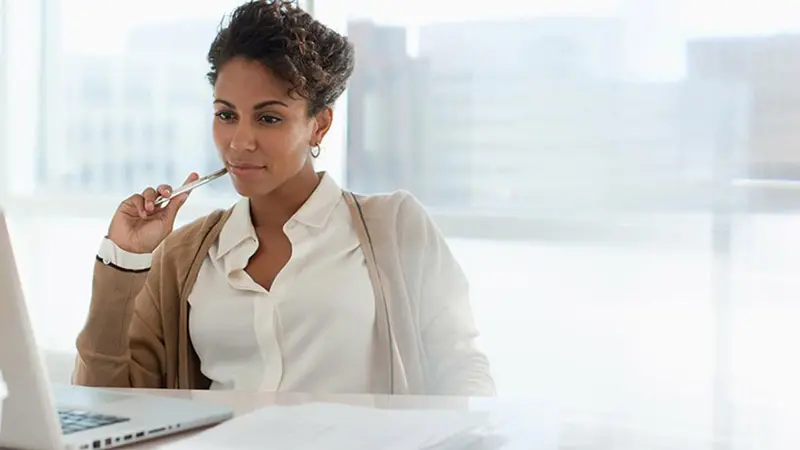 Woman holding pen while sitting and watching a video on her laptop