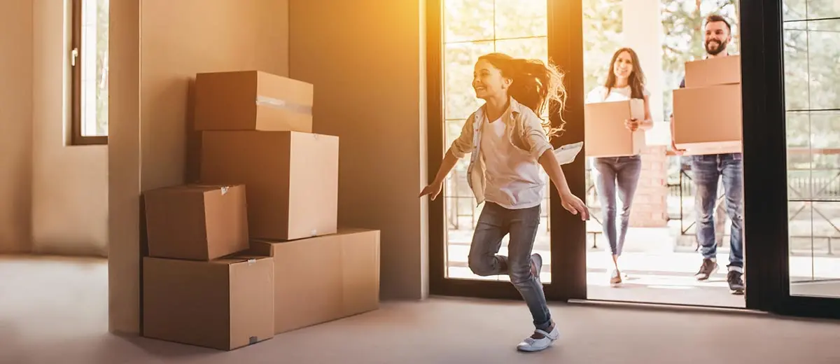 a child running into her new home with her parents carrying moving boxes behind her