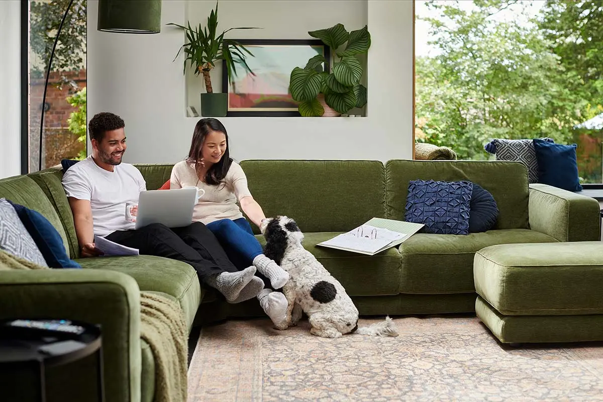 man and woman on a green couch petting a black and white dog