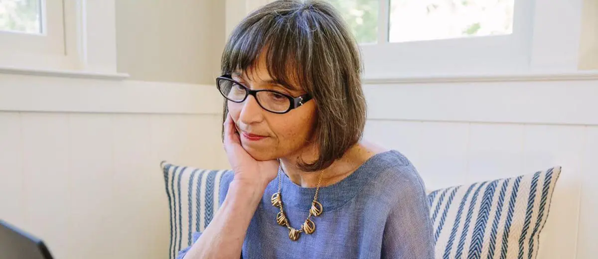 a woman wearing glasses, pensively looking at a laptop