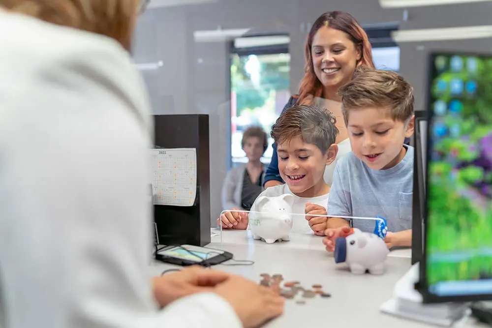 young boys at a bank teller window with piggy banks