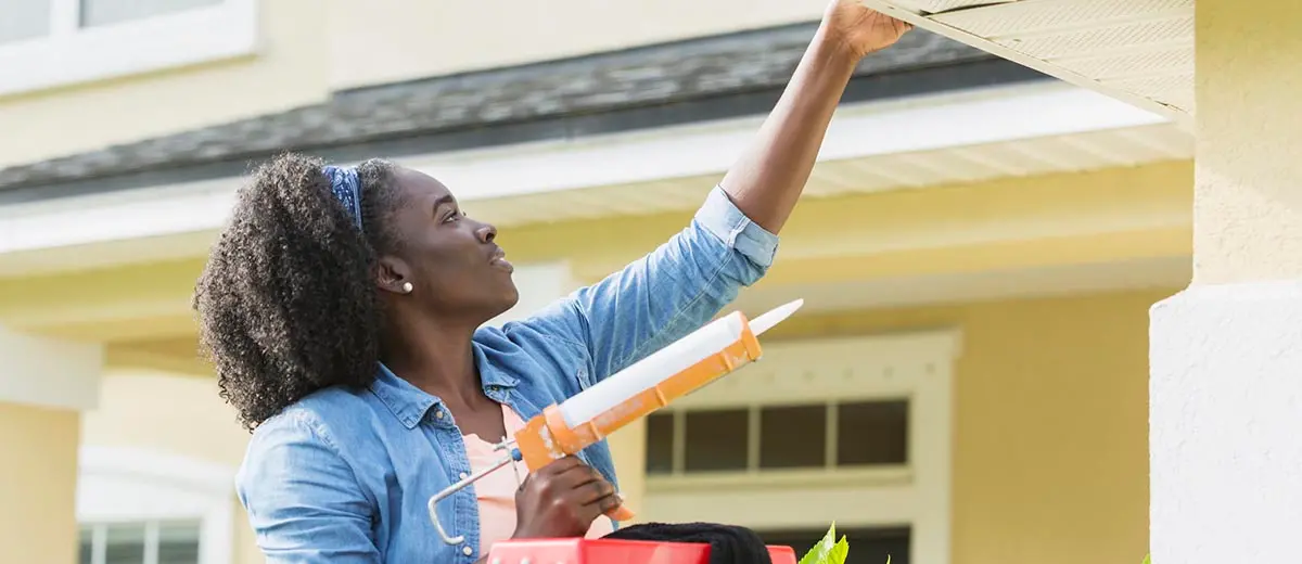 a woman in a blue shirt holding a caulk gun and repairing her home