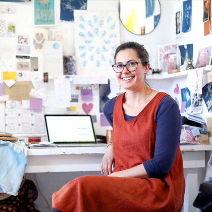 Woman sitting at a desk in front of her computer in her workshop.