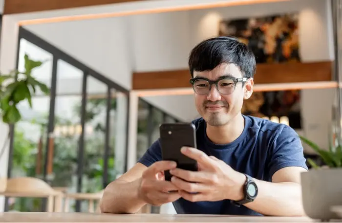 Man sitting at a table focused on a phone held with both hands, representing using Zelle