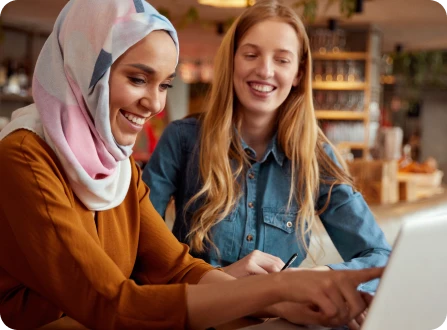 Two students in a coffee shop working together using a laptop