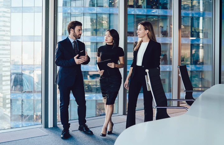Two women and a man who are wearing suits discussing wealth in a boardroom