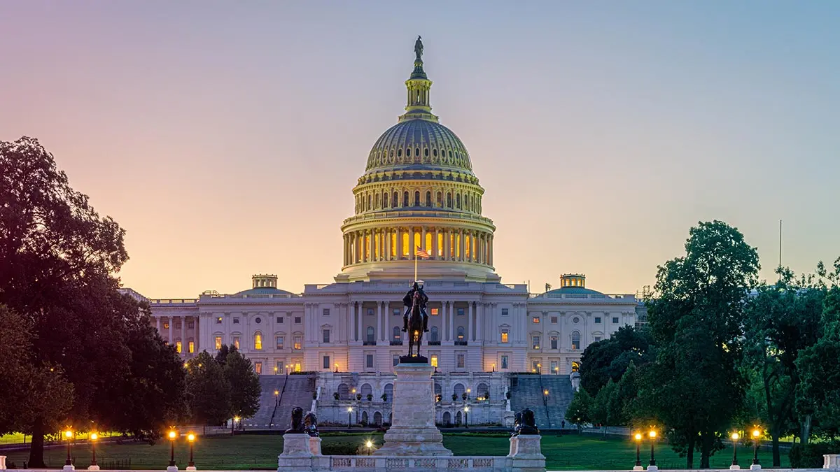 The U.S. Capitol building at twilight, featuring a statue in the foreground and trees surrounding the area.