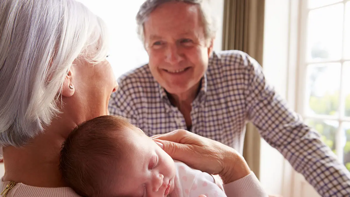 grandmother holding newborn while grandfather looks on