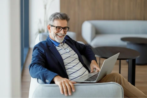Smiling middle aged man with a beard researching retirement planning on his laptop  