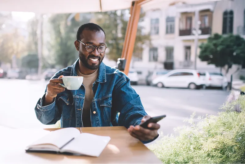 Man outdoors drinking coffee and looking at his phone