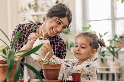 Mother helping her daughter water a house plant