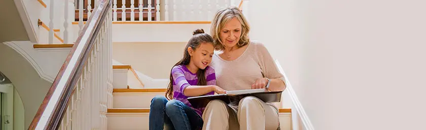 grandmother and granddaughter sitting on steps looking at photo album together