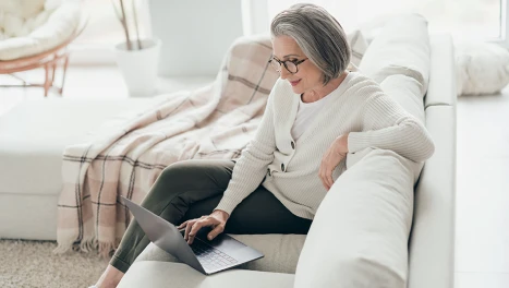 Older single woman using a laptop while sitting on her couch as she researches retirement options  