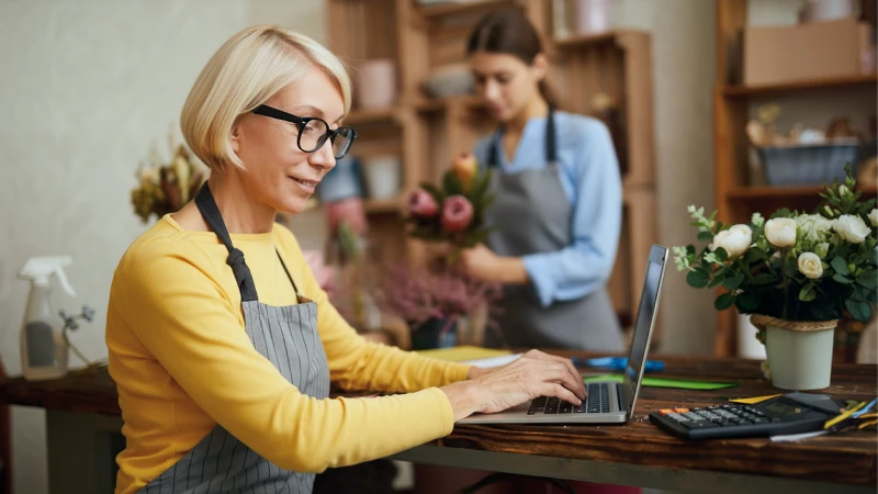 Business owner wearing an apron and typing on a laptop as she orders flowers for her business  