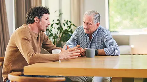 Older man and his son sitting at a kitchen table discussing wealth management