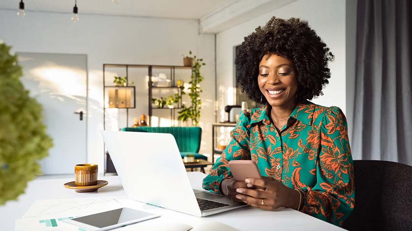 woman looking at phone while sitting in front of laptop