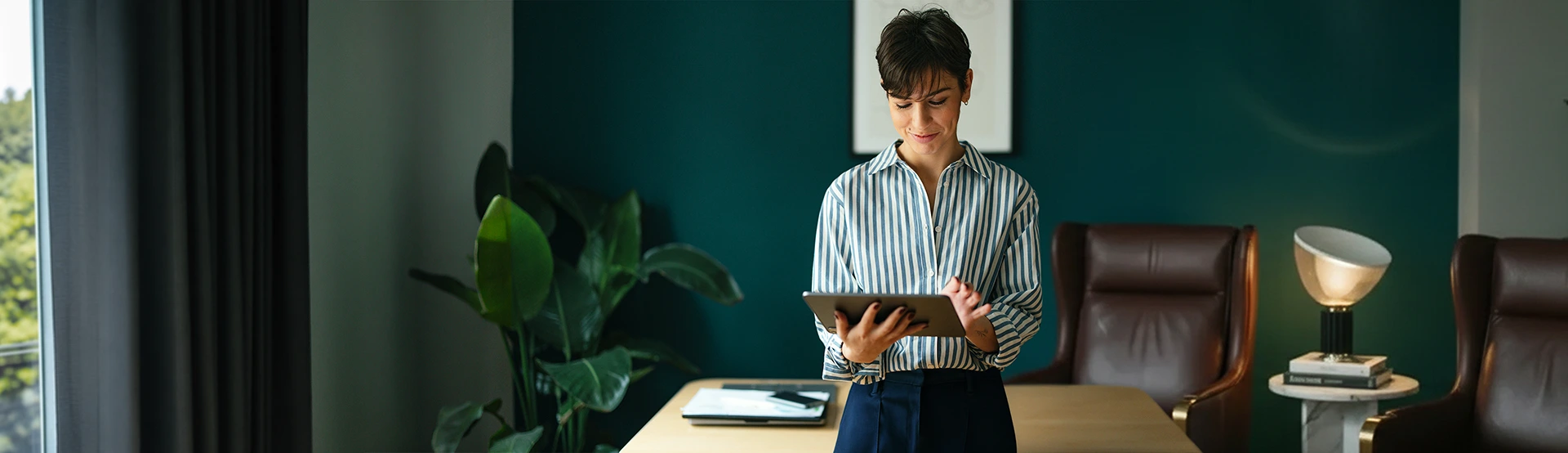 Young woman standing in front of her desk in her office and browsing on her tablet device for wealth management services