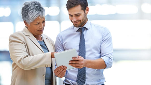 A person holding a tablet while another person stand next to them and points at the tablet