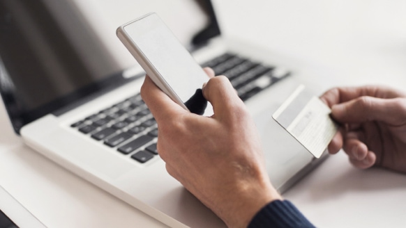 A hand holding a mobile phone over a laptop keyboard