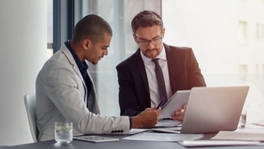 Two men collaborating on a tablet and computer