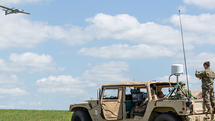 Army soldiers sitting in a Humvee in an open field as a large military plan flies overhead.