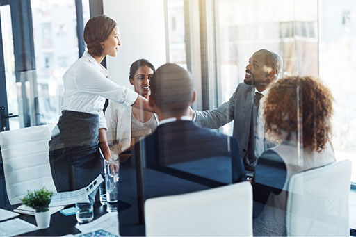 Five professional business people in a conference room, two of them shaking hands.