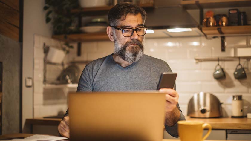 middle aged man looking at phone while sitting in front of computer